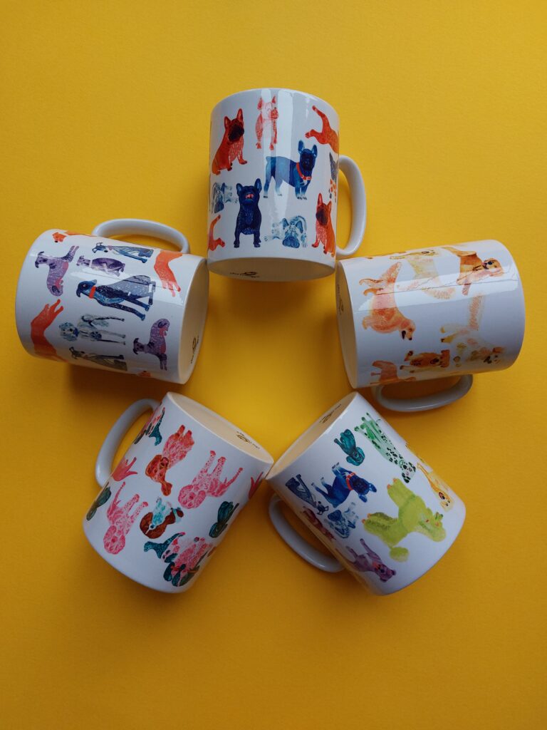 5 mugs on a yellow background in a star formation. Each mug has a different breed of dog colourful pattern illustrated on them. There's a sighthounds, french bulldogs, lots of different breeds (in the colours of the rainbow) , golden retrievers and spaniels.