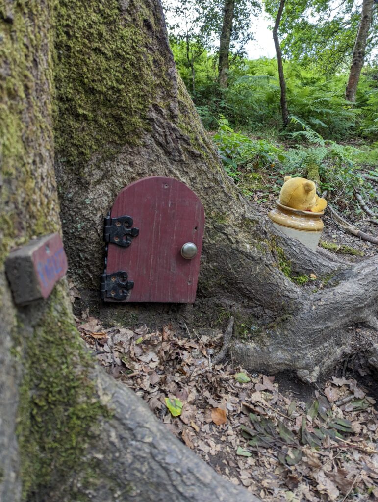 A picture of Ashdown forest with Winnie the Pooh's door in the foreground with Winnie face down in a pot of hunny
