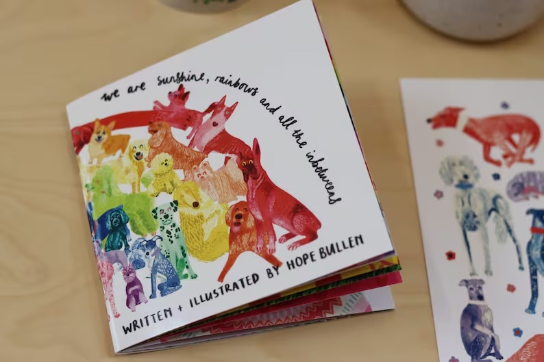 A picture of Hope Bullen's Children's Picture Book, We are sunshine, rainbows and all the inbetweens - the front cover has illustrated dogs in the format of a rainbow.