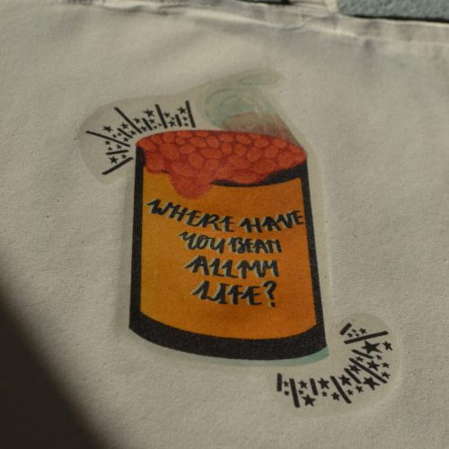A natural coloured tote bag with long handles, featuring a black and bright yellow baked beans can, with bright orange baked beans spilling out of the top, which has the phrase "Where Have You Bean All my Life" on the front. There are little black stars and lines in the background in the direction of the can. Size - 380 x 420mm, £12.50 including P+P.